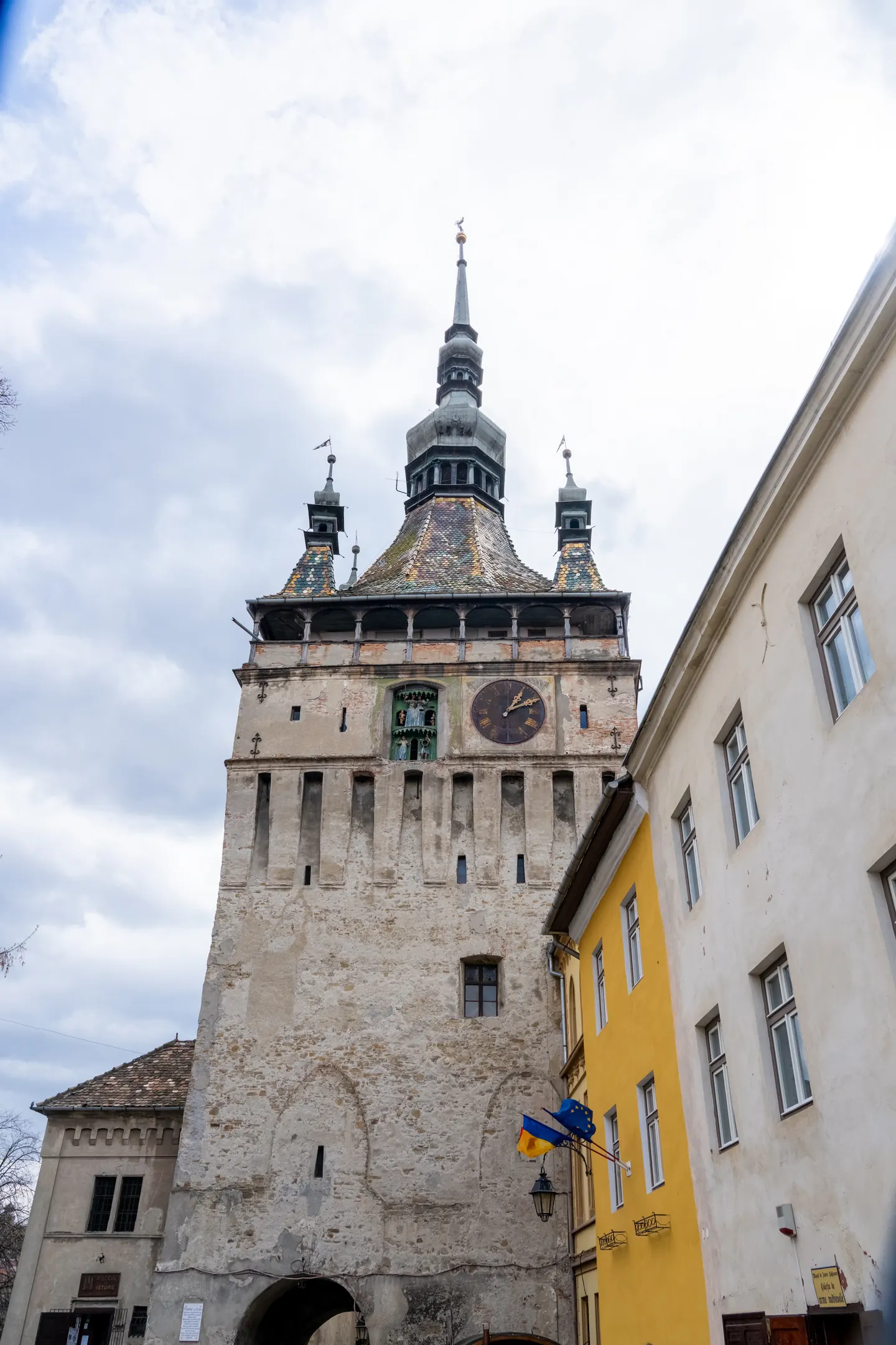 A segesvári Óratorony színes tetőcserepekkel és a szomszédos épület sárga homlokzatával